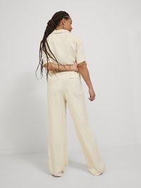 Completo di colore crema composto da un top a maniche corte e pantaloni a gamba larga, realizzato in un tessuto liscio con dettagli minimi.