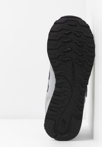 Schwarze Gummisohle mit strukturiertem Profil, hellgraues Synthetik-Obermaterial mit Mesh-Akzenten, mit einem New Balance Logo an der Seite.