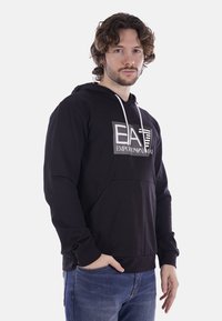 Felpa nera con cappuccio caratterizzata da una stampa del logo frontale grigia. Materiale morbido, tasca a marsupio e cappuccio con cordino. Vestibilità casual e polsini a costine.