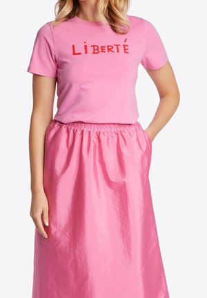 Różowa bawełniana koszulka z czerwonym napisem "LIBERTÉ", połączona z długą, błyszczącą różową spódnicą z elastyczną talią i bocznymi kieszeniami.
