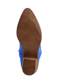 Zapato azul de ante con punta afilada, suela marrón texturizada y tacón bajo. La parte superior presenta costuras y un detalle de cremallera en el lateral.