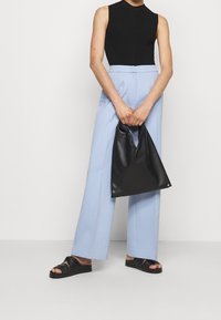 Czarny top bez rękawów, jasnoniebieskie spodnie z wysokim stanem, czarna skórzana torebka w kształcie trójkąta oraz czarne sandały na płaskiej podeszwie z fakturowanymi paskami.