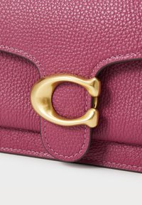 Sac à main en cuir textured violet avec un fermoir en métal doré, présentant un design lisse et arrondi ainsi que des accents cousus pour le détail.