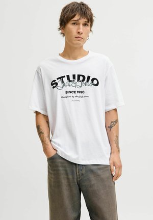 Weißes Baumwoll-T-Shirt mit schwarzem grafischem Textdesign, auf dem "STUDIO Jack & Jones SINCE 1990" steht. Kurze Ärmel, lockere Passform, Rundhalsausschnitt.
