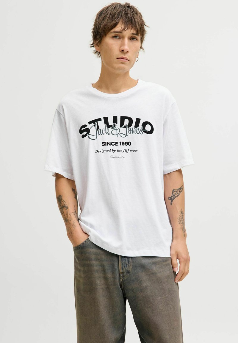 Biały bawełniany t-shirt z czarnym tekstem graficznym "STUDIO Jack & Jones SINCE 1990". Krótkie rękawy, luźny fason, okrągły dekolt.