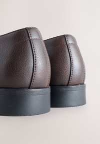 Pruunidest nahast pahkluu saapad tekstuurse viimistlusega, kontrastsete õmblustega ja musta kummist tallaga. Kujundatud ümarate tagumiste osade ja tugevast ehitusest.