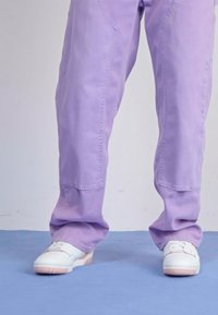 Pantaloni largi mov din bumbac, cu o textură netedă, asortați cu adidași albi cu accente roz pe tălpi.