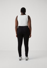 Vaqueros negros ajustados de cintura alta, combinados con una camiseta sin mangas blanca de canalé. Presentan una textura suave y bolsillos traseros estándar.