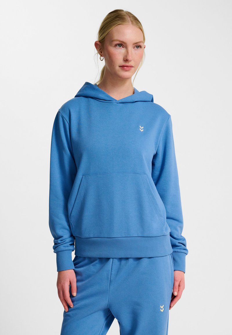 Blå hoodie i mjukt material, med en framficka, ribbad ärmslut och nederkant samt en liten guldig logga på bröstet. Matchande byxor.