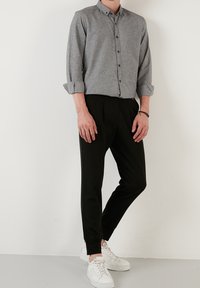 Grijs knoopshirt met kraag, opgerolde mouwen; gecombineerd met zwarte taps toelopende broek en witte sneakers. Soepele texturen, eenvoudig ontwerp.