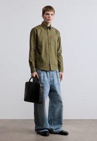 Πουκάμισο σε ελιά πράσινο με κουμπιά, φαρδιά τζιν παντελόνια σε ανοιχτό μπλε, μαύρη δερμάτινη τσάντα και μαύρα παπούτσια. Απλός σχεδιασμός, χωρίς σχέδια ή διακοσμήσεις.