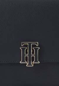 Surface en cuir texturé noir avec un détail de logo double T et H en émail noir et ton or centré.
