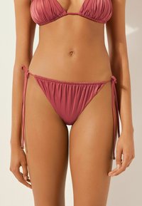 Bikini-set i mauve med en strukturerad tyg. Toppen har plisserade kupor, medan botten har justerbara snören på sidorna.