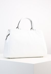 Biała skórzana torebka o usztywnionym kształcie, z dwoma okrągłymi uchwytami, srebrnymi elementami metalowymi i gładką fakturą.