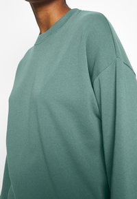 Grön sweatshirt i mjukt tyg, med rund halsringning, sänkta axlar och avslappnad passform. Strukturerad, avslappnad design.