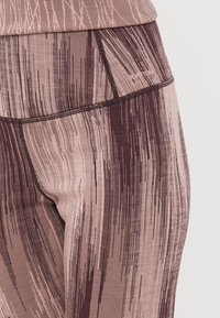 Leggings de cintura alta com um padrão de riscas verticais a mistura de rosa claro e castanho, fabricadas a partir de um tecido elástico e respirável.