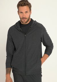 Felpa grigia con zip, dal tessuto morbido, maniche lunghe e design aderente. Presenta un cappuccio con coulisse e un discreto logo sul petto.