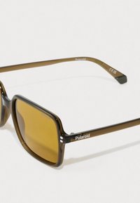 Rjave kvadratne sončne naočnike s okvirjem iz želvje lupine, rumenimi lečami in logotipom Polaroid na ročaju. Imajo sijoč zaključek.