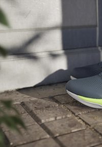 Light gray and yellow athletic shoes on textured stone pavement with shadowed concrete wall in soft natural light.