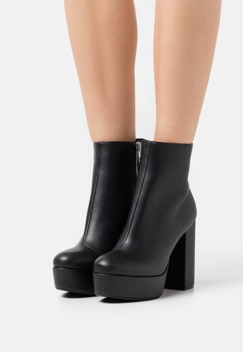 Bottes à plateformes en cuir noir avec un talon carré haut, dotées d'une fermeture éclair sur le côté et d'une texture lisse mate.