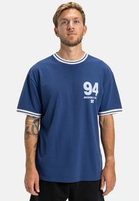 Námornícky modré bavlnené tričko s okrúhlym výstrihom, bielymi pruhmi a potlačeným číslom "94" s brandingom na prednej strane.