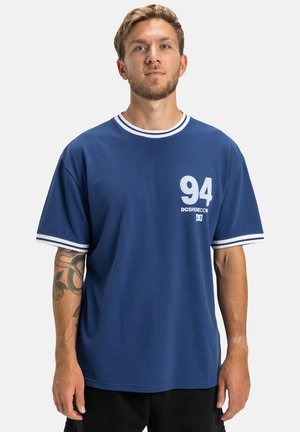 T-shirt en coton bleu marine avec un col rond, des accents rayés blancs et un numéro imprimé "94" avec un logo sur le devant.