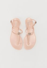 Sandales en plastique rose avec une semelle plate, arborant un design de tongs minimaliste et un accent logo métallique circulaire. Bride de cheville ajustable incluse.