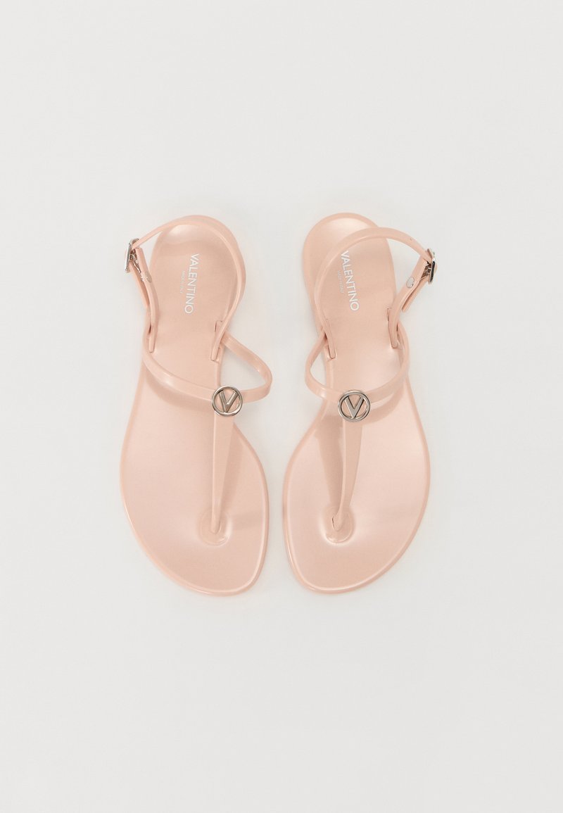 Sandales en plastique rose avec une semelle plate, arborant un design de tongs minimaliste et un accent logo métallique circulaire. Bride de cheville ajustable incluse.