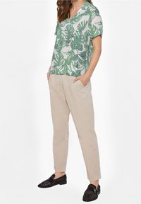 Top a maniche corte con stampa di foglie verdi su sfondo bianco, abbinato a pantaloni beige a sigaretta e mocassini neri intrecciati.