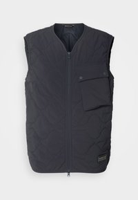 Vesta neagră matlasată cu fermoar frontal, o buzunar cu capse pe pieptul stâng și o textură netedă. Logo-ul Barbour pe partea dreaptă jos.