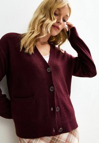 Cardigan bordeaux con scollo a V, maniche lunghe, due tasche frontali e bottoni scuri. Tessuto morbido e-texturizzato con una vestibilità rilassata.