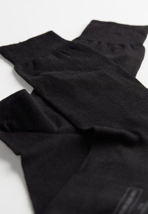 Černé pletené návleky na nohy vyrobené z měkkého materiálu, se žebrovaným manžetovým lemem a hladkým povrchem. Ozdobené malou značkovou etiketou.