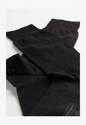 Mangas de pierna negras de punto hechas de una tela suave, con un puño acanalado y una textura lisa. Acentuadas con una pequeña etiqueta de marca.