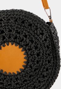 Okrągła czarna torebka szydełkowa z teksturowaną powierzchnią i pomarańczowym skórzanym akcentem na środku, z odpinanym paskiem.