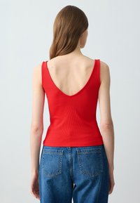 Top in cotone a coste rosso con schiena a V profonda, caratterizzato da spalline larghe. Abbinato a jeans in denim blu a vita alta.