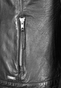 Svart läderjacka med en sektion som visar en dragkedjeficka, silverfärgad dragkedja, slät yta och subtila veck i lädret.