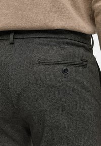 Pantalones de cuadros grises confeccionados con tela texturizada, con un bolsillo trasero con cierre de botón y un sutil detalle de marca.