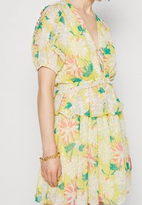 Květinové šaty s hlubokým výstřihem do V, krátkými nabíranými rukávy a vícevrstvým volánkem na spodním lemu. Vyznačují se žlutým pozadím s růžovými a modrými květinovými vzory.