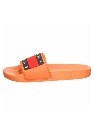 Orangefarbene Slide-Sandale mit einem rot-schwarzen Riemen mit den Buchstaben „TOMMY JEANS“ und dem geprägten Schriftzug „JEANS“ an der Seite der Sohle.
