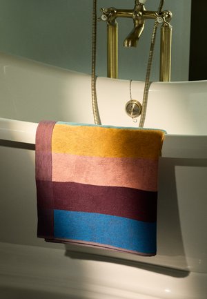 Flerfärgad handduk med horisontella ränder i nyanser av gult, rosa, lila och blått, tillverkad av texturerad tyg, hängande över ett badkar.
