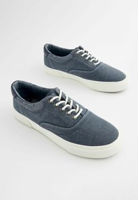 Blaue Segeltuch-Sneaker mit weißen Gummisohlen. Merkmale sind eine runde Zehenpartie, Schnürung, Metallösen und eine strukturierte Oberfläche.