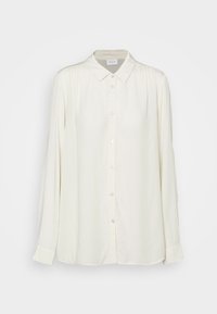 Blusa a maniche lunghe di un leggero color crema, realizzata in tessuto morbido, con colletto, chiusura frontale a bottoni e delicate pieghe sulle spalle.