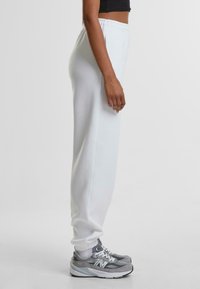 Witte joggingbroek met een relaxte pasvorm, gemaakt van zachte stof, met een elastische tailleband, afgeknipte enkels en zijzakken. Gepaard met grijze sneakers.