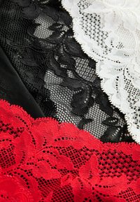 Spitzenstoffe in Schwarz, Weiß und Rot mit floralen Mustern und feinen Texturen, geschichtet mit kontrastierenden Farben und Designs.