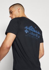 Čierne tričko z bavlny, s modrou grafickou aplikáciou hôr, stromov a logom Columbia na chrbte. Krátke rukávy.