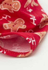 Czerwony materiał z wzorami piernikowych ludzików w odcieniach beżu i bieli. Gładka tekstura z zagiętym brzegiem ukazującym nadrukowany tekst i akcenty.