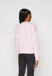 Svetlo roza sweatshirt s krojem okroglega izreza, spuščeni rameni in rebrastim robom. Ima bele stranske črte in mehak, teksturiran material.