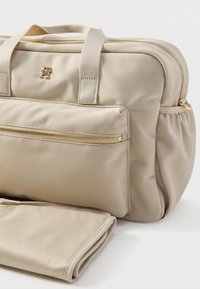 Beżowa torba na laptopa z nylonu z podwójnymi uchwytami na górze, przednią kieszenią na zamek, złotymi detalami i dołączonym składanym przewijakiem.