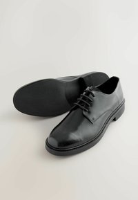 Schwarze Lederdressschuhe mit glatter Oberfläche, Schnürdesign, abgerundeter Spitze und strukturiertem Gummisohle mit leichtem Absatz.