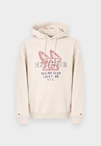 Beżowa bluza z kapturem z napisem "Tommy Hilfiger Racing Club Lucky .85 NYC" oraz skrzydlatym logo "H" w kolorze czerwonym i granatowym z przodu, z kapturem ze sznurkiem, elastycznymi mankietami.